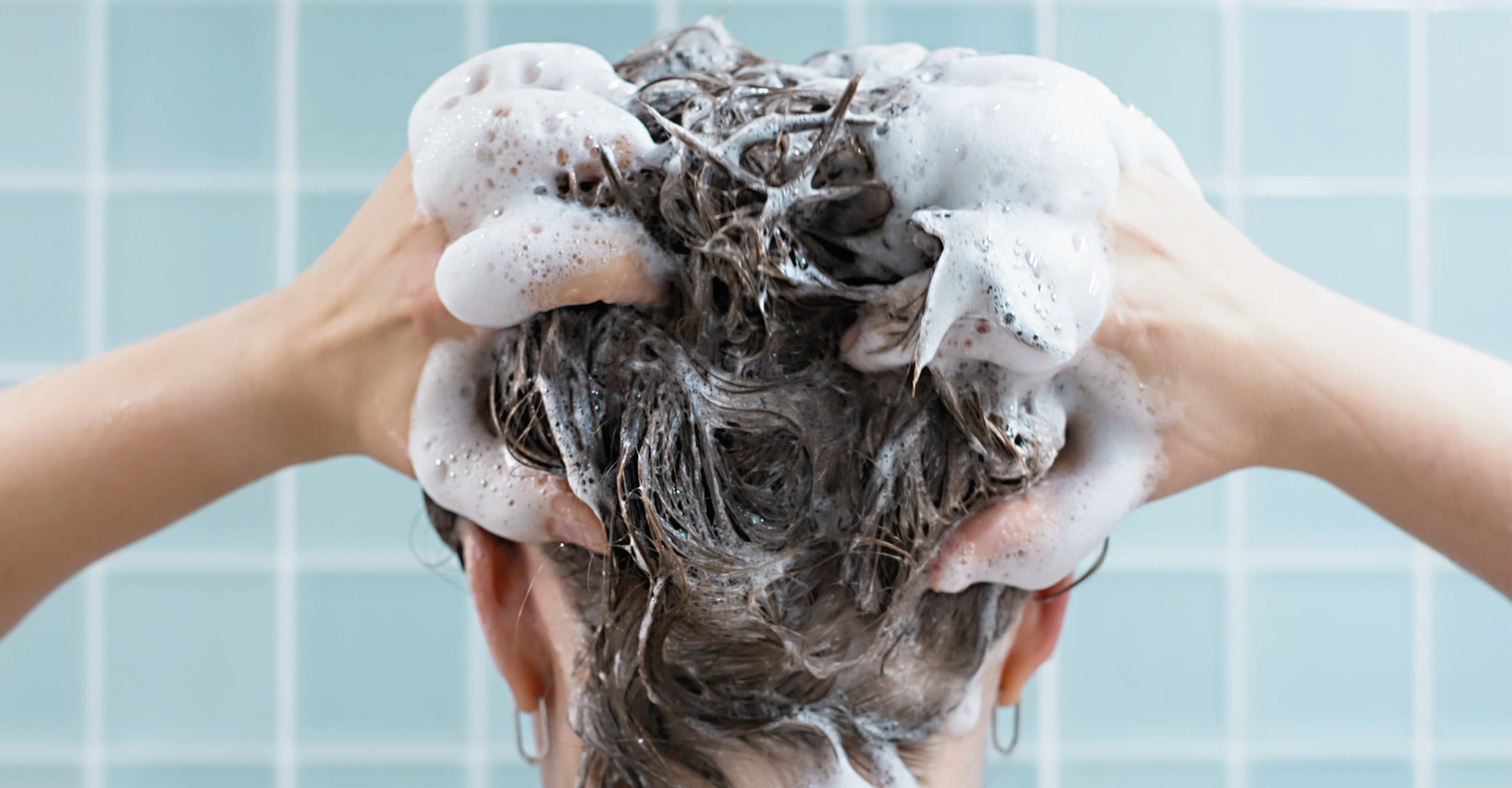 Ragazza mora, in doccia, con capelli corti, che si sta lavando con lo shampoo i capelli