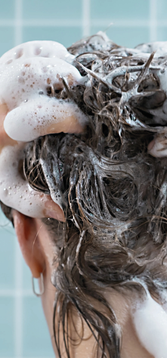 Ragazza mora, in doccia, con capelli corti, che si sta lavando con lo shampoo i capelli